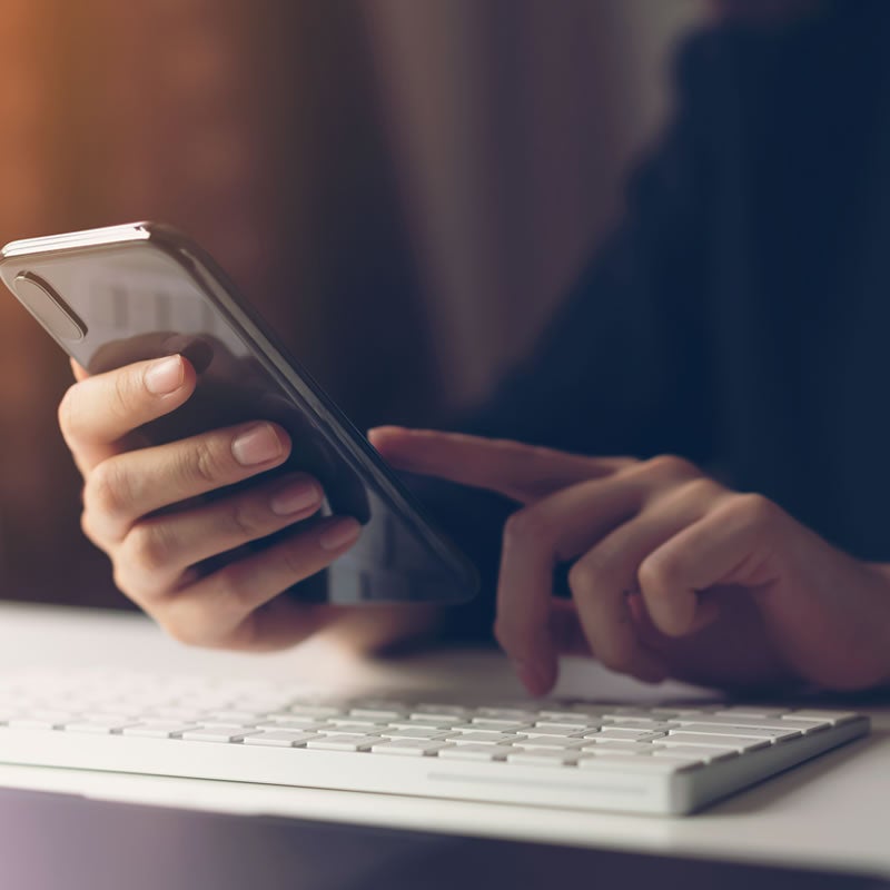 Hands over keyboard with mobile phone